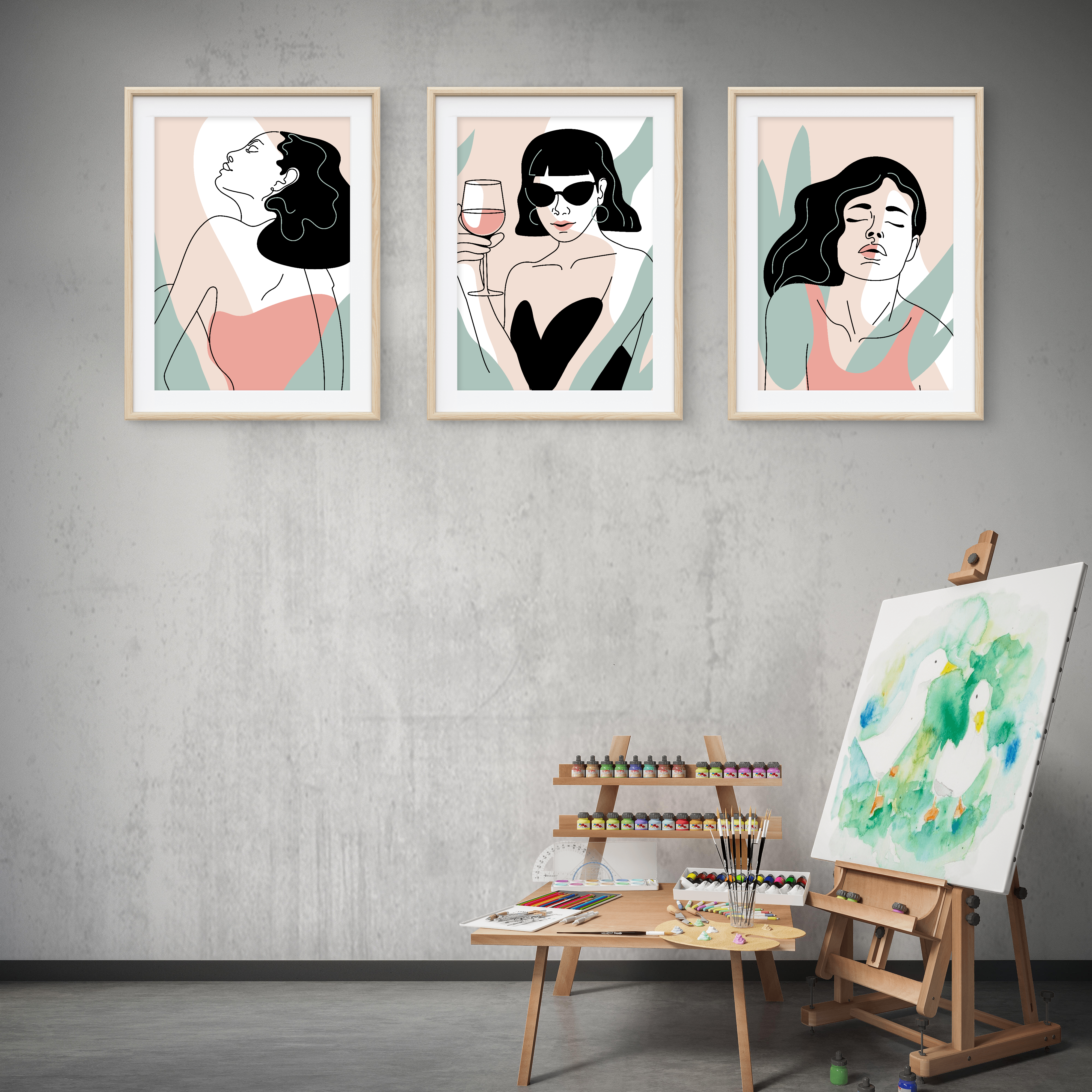 Three framed artworks of women on a wall with an easel and painting supplies below.