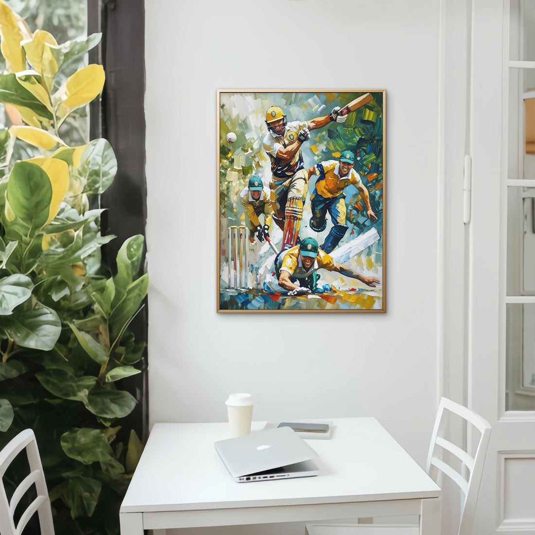Colorful painting of a cricket match on a wall above a desk with a laptop and cup.